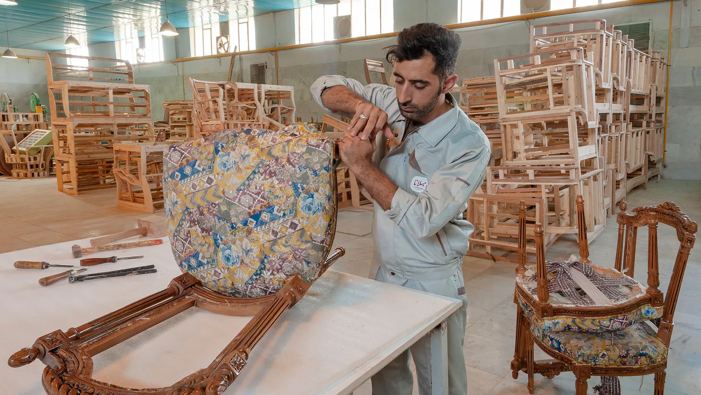 استادکار مبلانا در حال رویه‌کوبی کلاف مبل کلاسیک در کارگاه